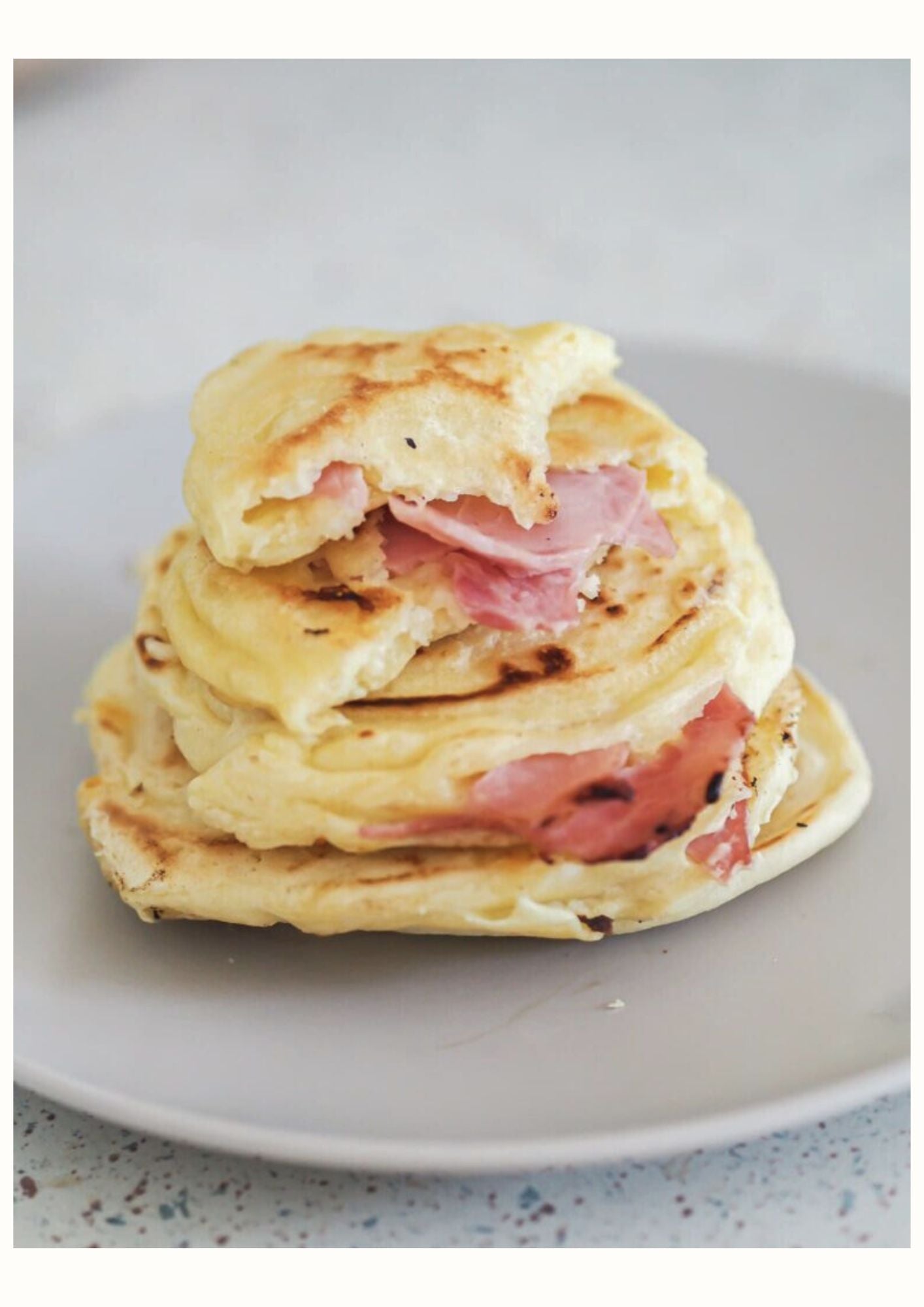 Pancakes fourrés au jambon et fromage empilés sur une assiette beige
