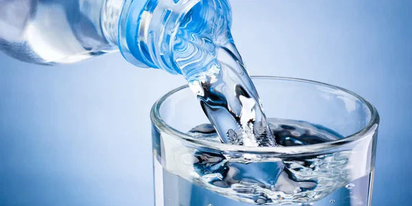 Bouteille d'eau versant dans un verre, symbole de l'hydratation et digestion essentielles pour le bien-être