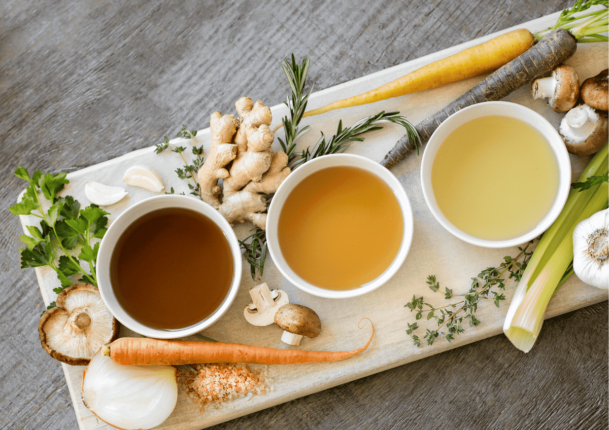 Tout est bon dans le bouillon ! Trois bols de bouillon avec légumes frais et herbes aromatiques sur planche en bois
