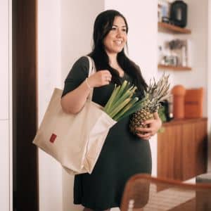 Femme souriante tenant un Tote Bag et des légumes frais avec un ananas dans l&